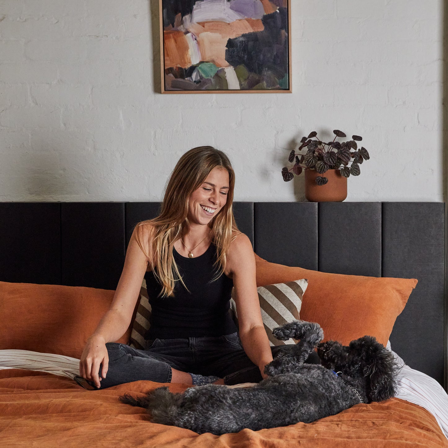 Woman and dog comfortably sitting on top of the assembled Yona bed base and headboard