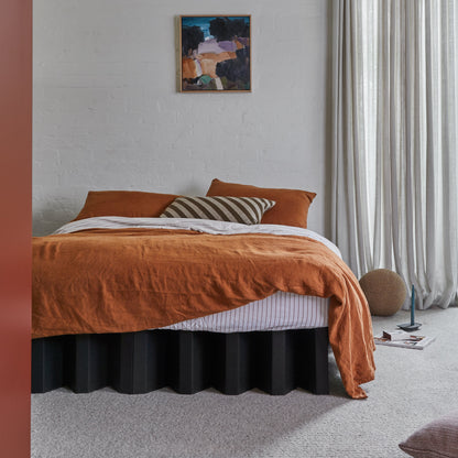 Yona Cardboard Bed in black finish styled with rust-colored bedding and striped pillow in a modern bedroom with neutral decor